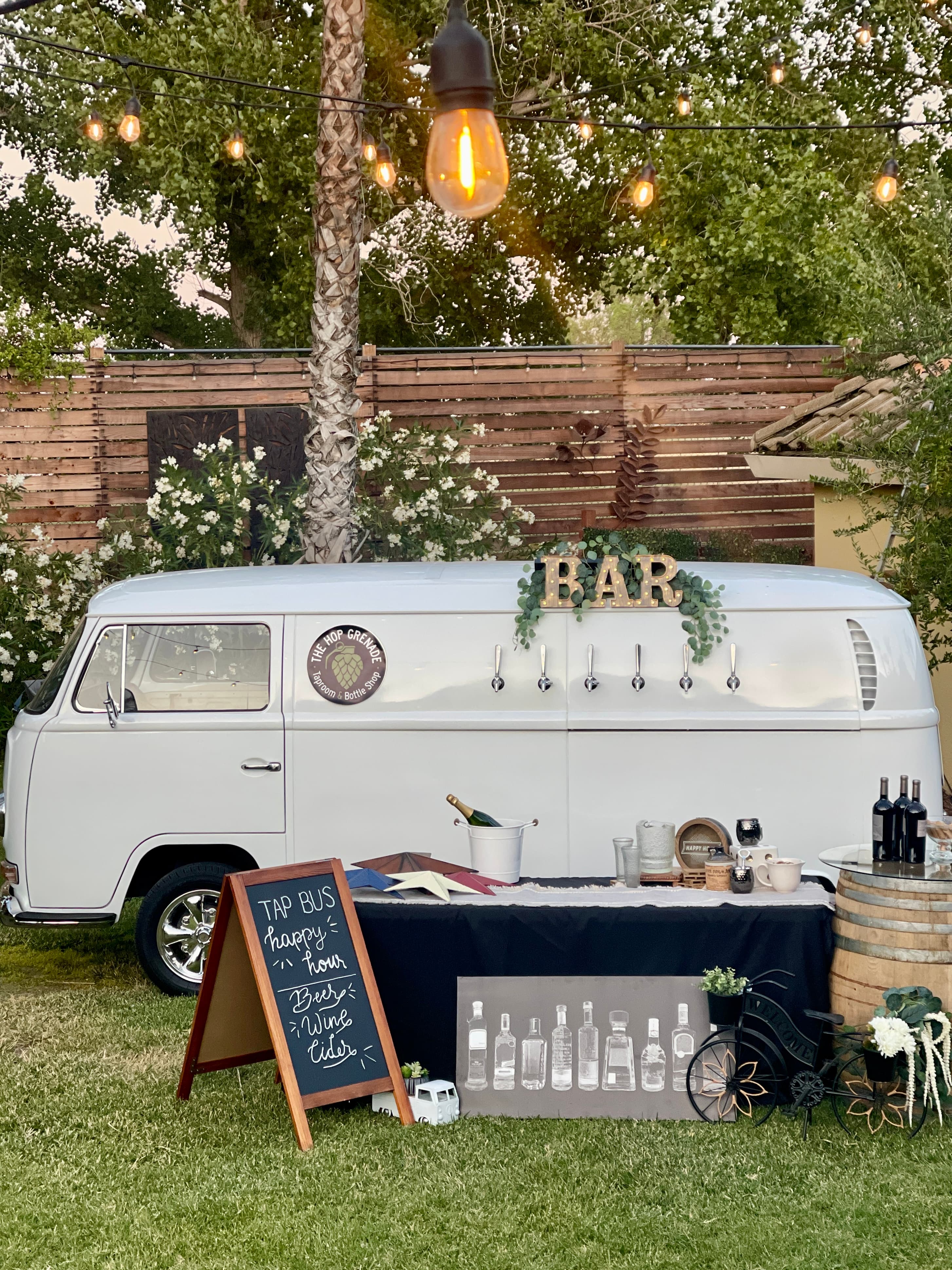 White vintage VW bus mobile bar with beer taps, string lights, and happy hour chalkboard.